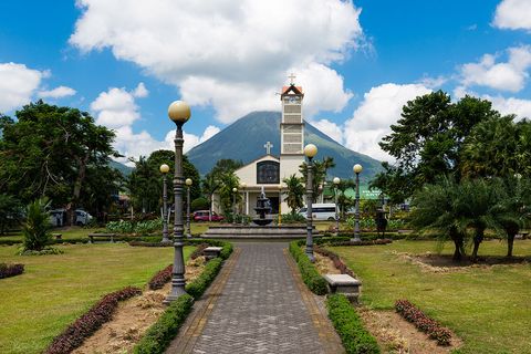 The town of La Fortuna — a park pathway, church, and Arenal Volcano in the background.