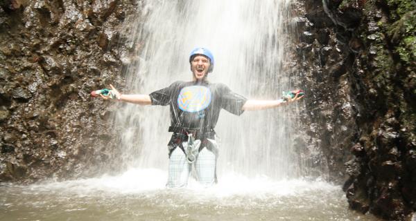 Arenal Water Activities Image: A man stands with his arms out in victory under a waterfall rappel.