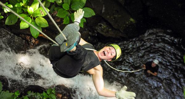 Arenal Water Activities Image: A woman laughs with arms outstretched whilst upside down, rappelling.