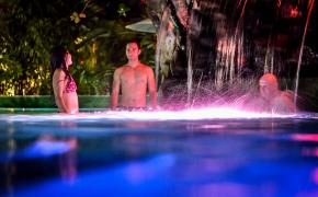 Arenal Hot Springs Image: Three people enjoy the illuminated pools of Paradise Hot Springs at night.